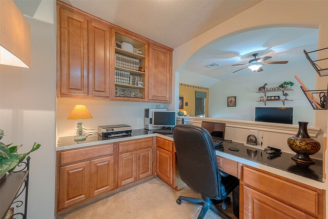 home office featuring ceiling fan, a textured ceiling, built in desk, light colored carpet, and vaulted ceiling