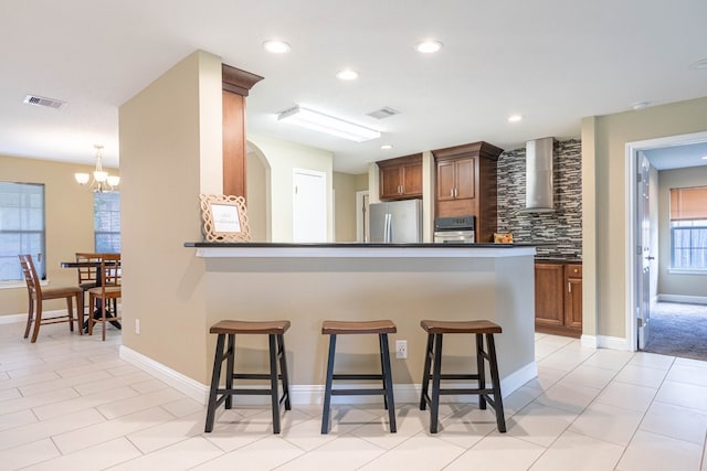 kitchen with a kitchen breakfast bar, wall chimney range hood, appliances with stainless steel finishes, and an inviting chandelier