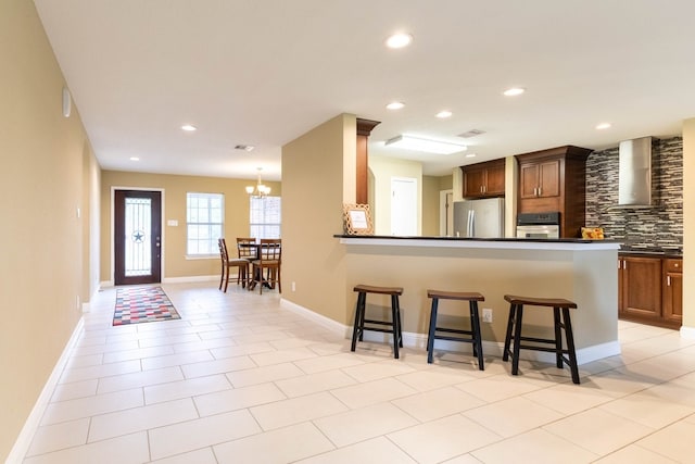 kitchen with light tile patterned floors, appliances with stainless steel finishes, wall chimney exhaust hood, and a breakfast bar area