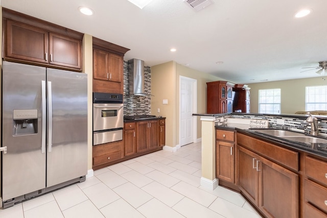 kitchen with ceiling fan, appliances with stainless steel finishes, decorative backsplash, wall chimney range hood, and sink