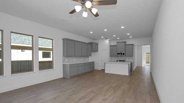 kitchen featuring a kitchen island with sink, decorative backsplash, and gray cabinets