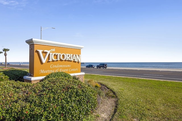 community sign featuring a lawn and a water view