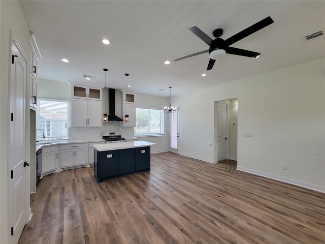 kitchen with a center island, ceiling fan with notable chandelier, white cabinets, stainless steel stove, and wall chimney exhaust hood