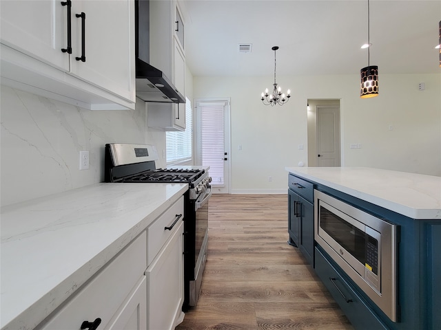 kitchen with appliances with stainless steel finishes, white cabinetry, light wood-type flooring, decorative light fixtures, and wall chimney range hood