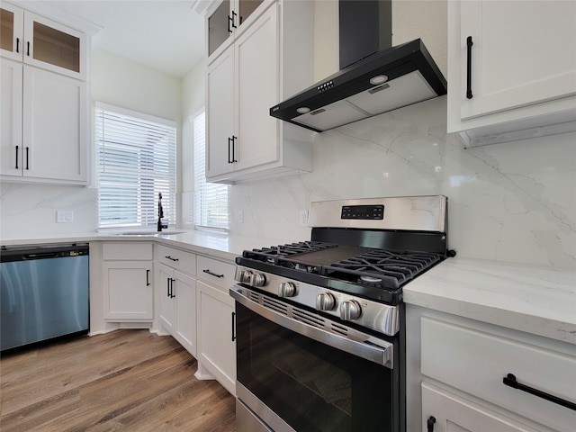 kitchen featuring wall chimney exhaust hood, stainless steel appliances, white cabinets, and light hardwood / wood-style floors