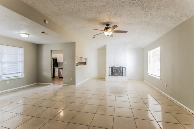 unfurnished living room with ceiling fan, a textured ceiling, a fireplace, and light tile patterned floors