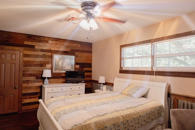 bedroom with wood walls, ceiling fan, and dark wood-type flooring