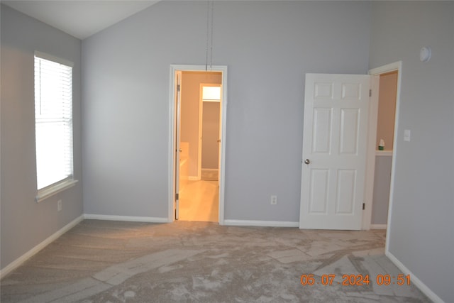 unfurnished bedroom featuring light colored carpet, ensuite bathroom, and high vaulted ceiling