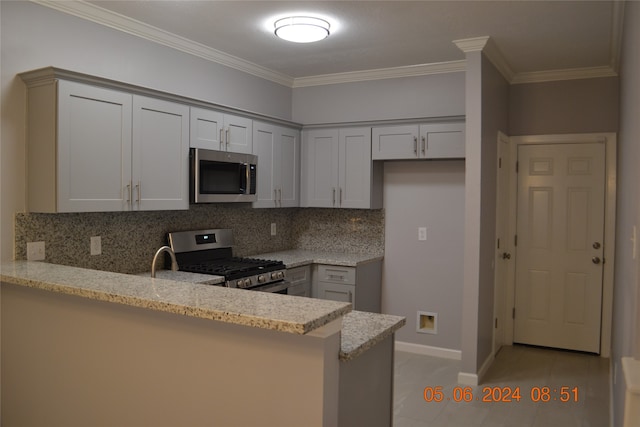 kitchen with appliances with stainless steel finishes, tasteful backsplash, kitchen peninsula, light stone countertops, and ornamental molding