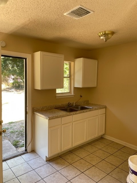 kitchen with white cabinets, light tile patterned floors, sink, and a textured ceiling