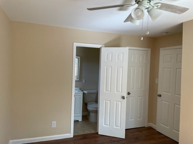 unfurnished bedroom featuring connected bathroom, ceiling fan, and dark wood-type flooring