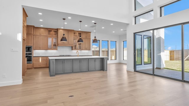 kitchen featuring stainless steel appliances, light countertops, backsplash, light wood-style floors, and a kitchen island with sink