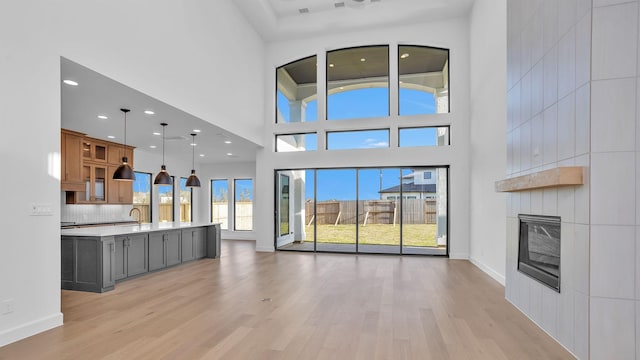 unfurnished living room with a large fireplace, a high ceiling, baseboards, and light wood finished floors