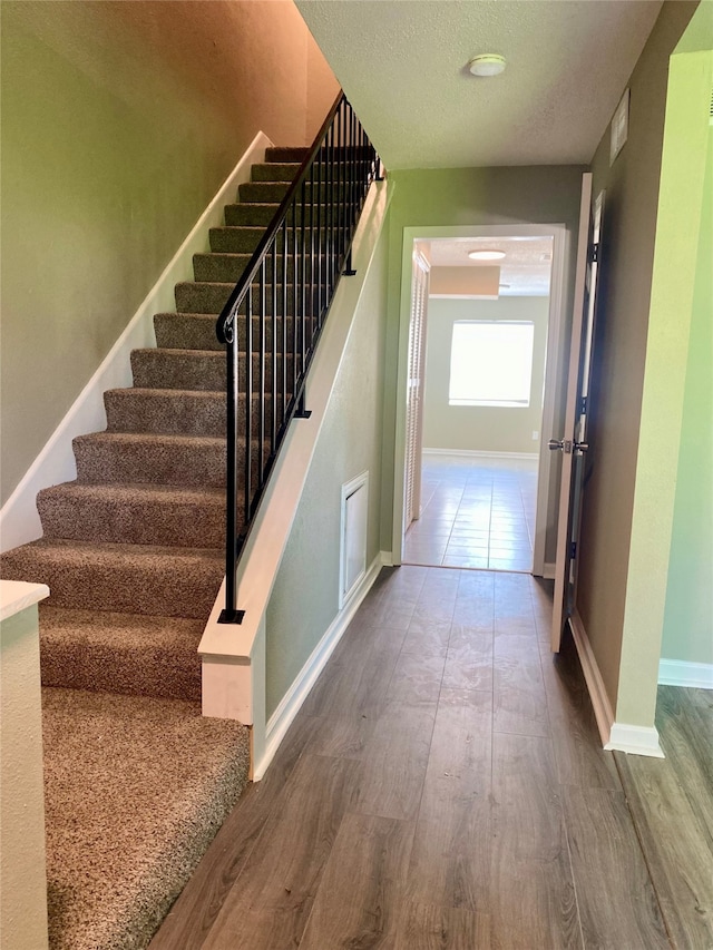 stairway with wood-type flooring and a textured ceiling