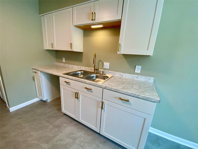 kitchen with white cabinets, light stone counters, light tile patterned floors, and sink