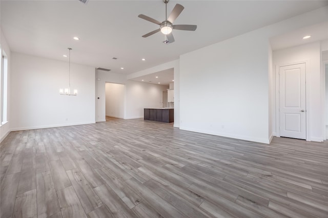 unfurnished living room featuring recessed lighting, baseboards, light wood finished floors, and ceiling fan with notable chandelier