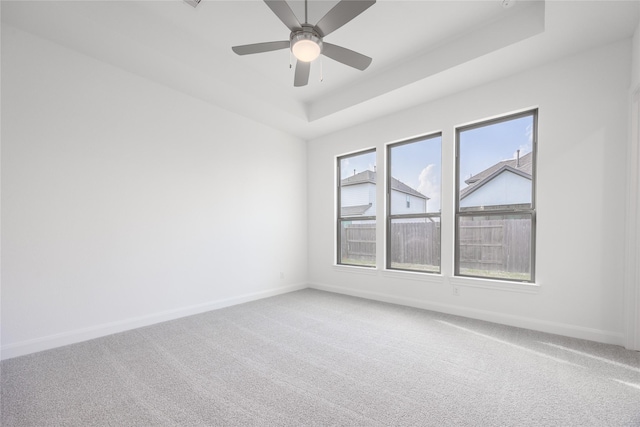 empty room with baseboards, a raised ceiling, light carpet, and ceiling fan