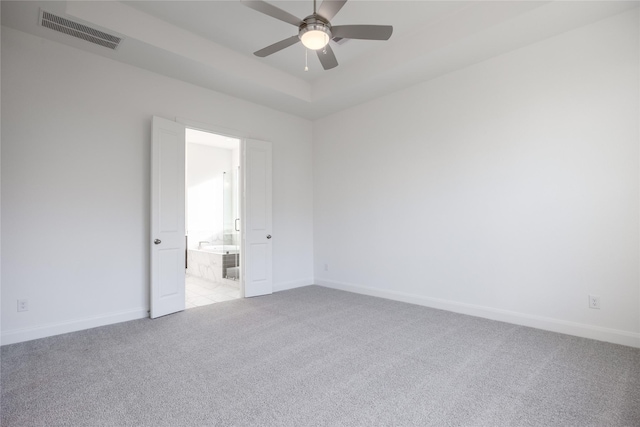 empty room featuring visible vents, baseboards, a tray ceiling, light carpet, and a ceiling fan