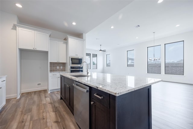 kitchen with a sink, tasteful backsplash, white cabinetry, stainless steel appliances, and light wood finished floors