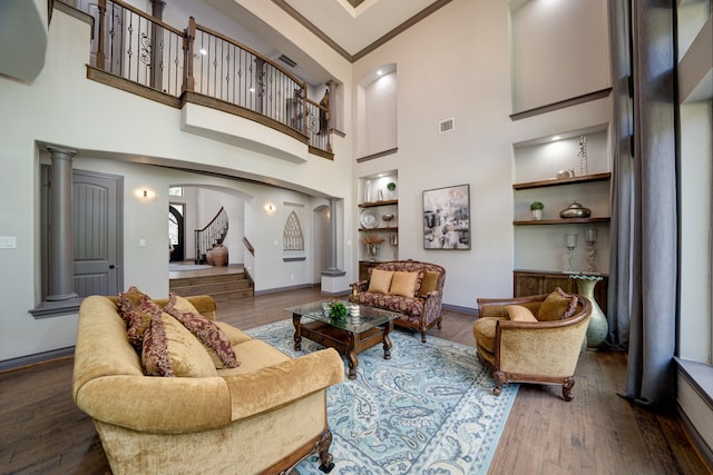 living room with a towering ceiling, decorative columns, built in features, and dark wood-type flooring