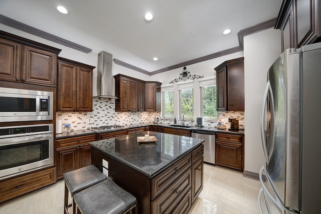 kitchen featuring appliances with stainless steel finishes, a breakfast bar area, a center island, sink, and wall chimney range hood