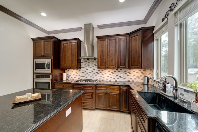 kitchen featuring sink, wall chimney exhaust hood, stainless steel appliances, ornamental molding, and dark stone countertops