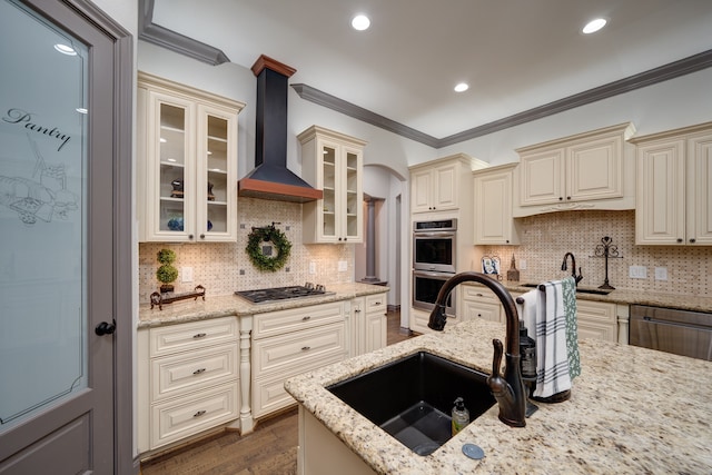 kitchen featuring appliances with stainless steel finishes, backsplash, cream cabinets, sink, and wall chimney range hood