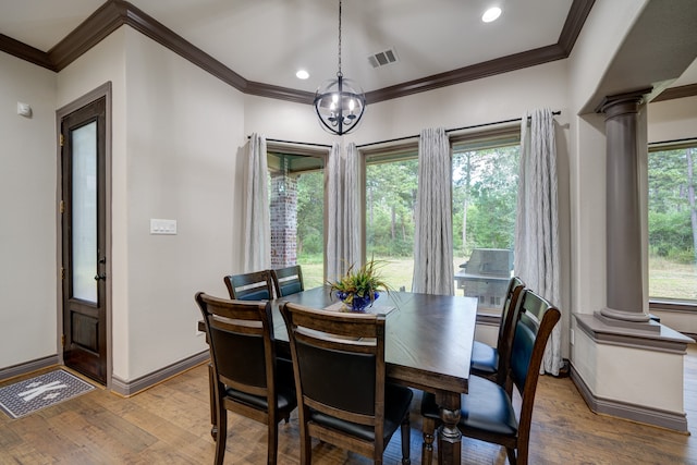 dining room with wood-type flooring, a notable chandelier, crown molding, and decorative columns