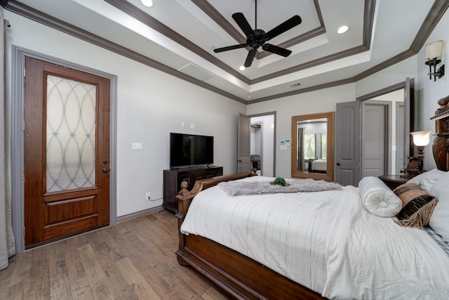 bedroom featuring ceiling fan, a tray ceiling, ornamental molding, and wood-type flooring