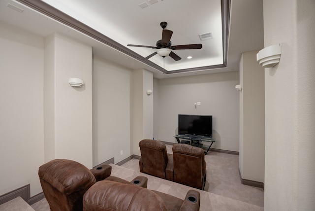 cinema room featuring a raised ceiling, ceiling fan, and light colored carpet