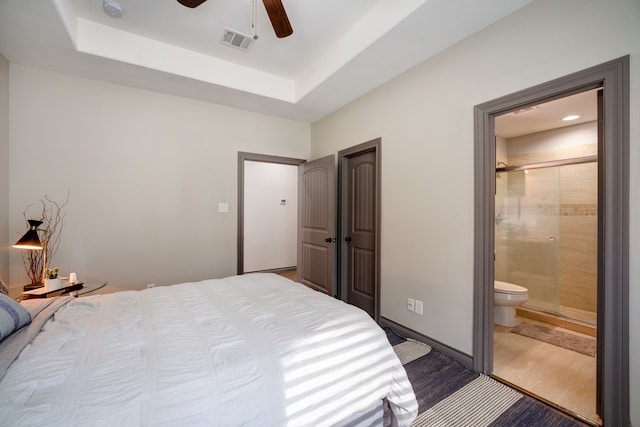 bedroom with a raised ceiling, ensuite bath, and ceiling fan