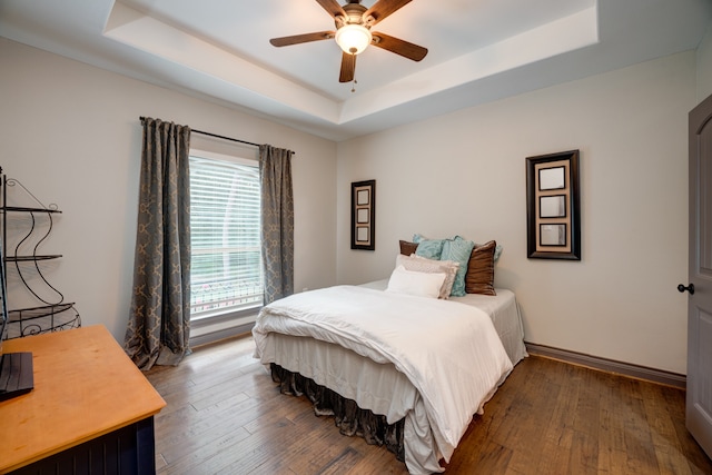 bedroom featuring ceiling fan, a raised ceiling, and dark wood-type flooring