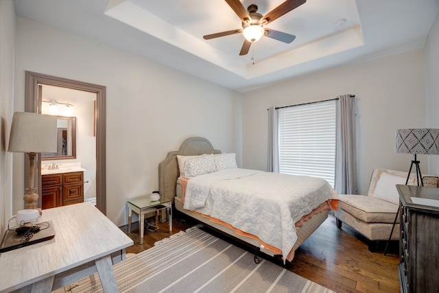 bedroom with a raised ceiling, ensuite bath, ceiling fan, and dark hardwood / wood-style flooring