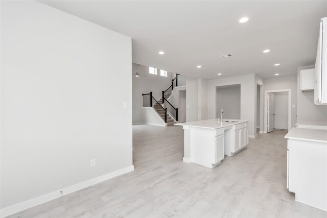 kitchen featuring light wood-type flooring, sink, an island with sink, and white cabinets