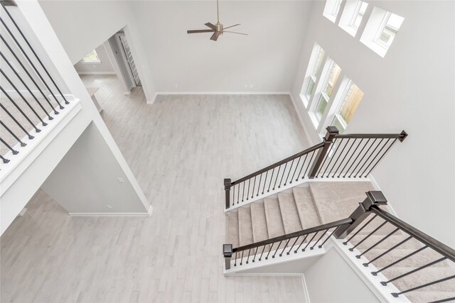 staircase with ceiling fan, hardwood / wood-style flooring, and a high ceiling