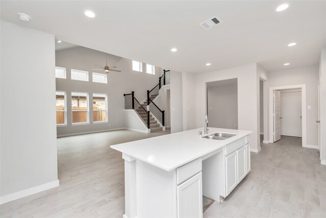 kitchen with light hardwood / wood-style floors, an island with sink, white cabinets, ceiling fan, and sink