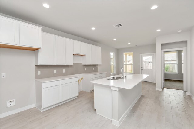 kitchen with light hardwood / wood-style floors, a kitchen island with sink, sink, and white cabinetry