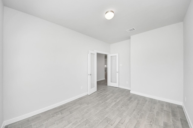 spare room with light wood finished floors, visible vents, and baseboards