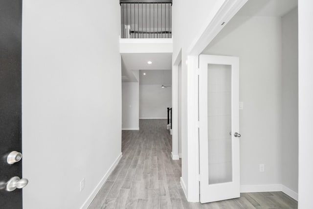 hallway featuring wood finished floors, baseboards, and a towering ceiling