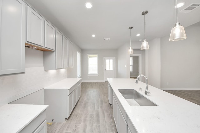 kitchen with a sink, decorative backsplash, visible vents, and light wood finished floors