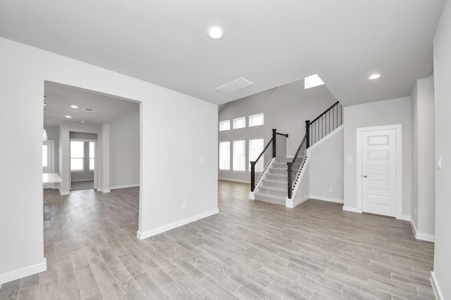 empty room featuring stairs, light wood-style flooring, and a healthy amount of sunlight