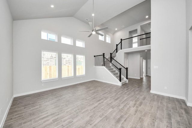 unfurnished living room featuring high vaulted ceiling, a ceiling fan, wood finished floors, baseboards, and stairs