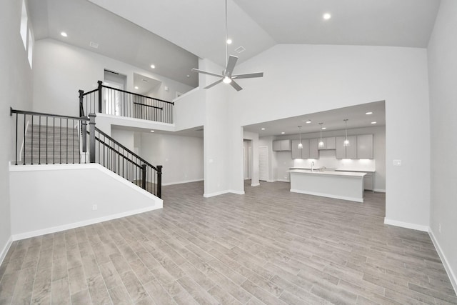 unfurnished living room featuring light wood-style flooring, a ceiling fan, recessed lighting, baseboards, and stairs