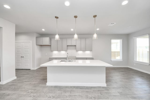 kitchen featuring visible vents, a center island with sink, light countertops, and a sink