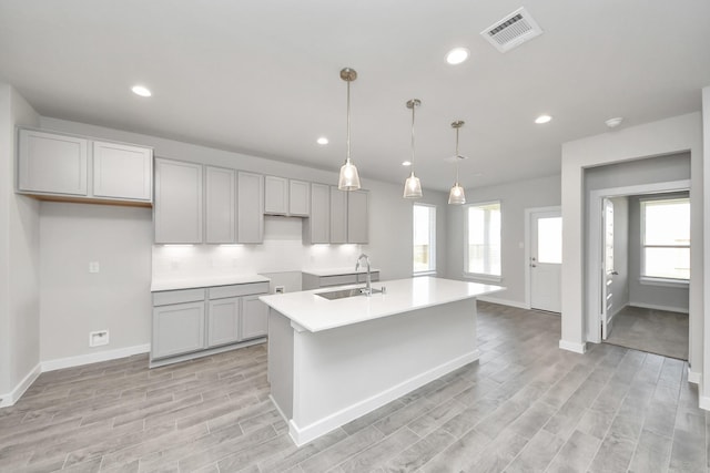 kitchen with a wealth of natural light, visible vents, a kitchen island with sink, a sink, and light wood finished floors