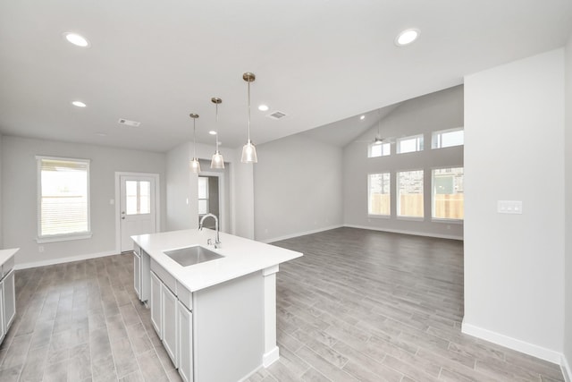 kitchen with a healthy amount of sunlight, a center island with sink, visible vents, a sink, and light countertops