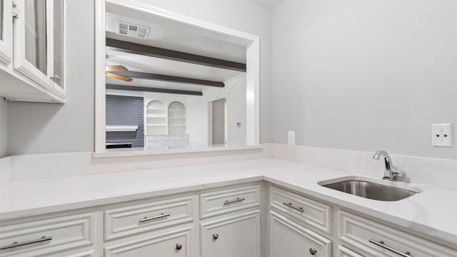 kitchen featuring beam ceiling, white cabinetry, sink, and ceiling fan