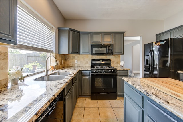 kitchen with light stone counters, light tile patterned floors, backsplash, black appliances, and sink