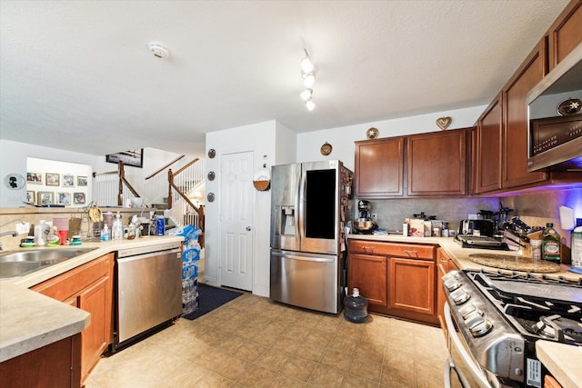 kitchen featuring light countertops, backsplash, a sink, appliances with stainless steel finishes, and brown cabinetry