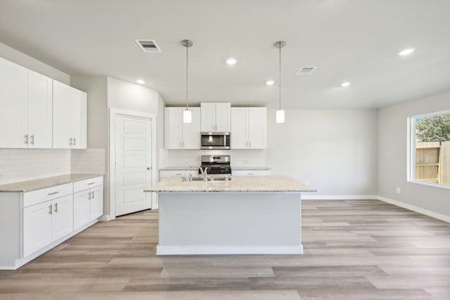 kitchen with pendant lighting, light hardwood / wood-style floors, white cabinetry, and appliances with stainless steel finishes